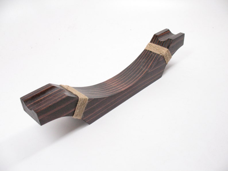 May include: A dark brown, wooden decorative object with a curved, angular design. The object is wrapped with twine at two points. The wood grain is visible, and the object has a smooth, polished finish. The object is likely a decorative piece.