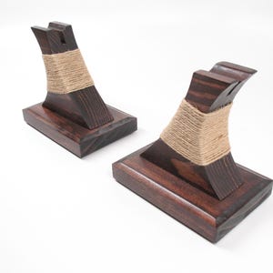 May include: Two dark stained wooden bookends with a curved design. Each bookend has a rectangular base and a curved support wrapped with natural twine. The bookends are displayed on a white background.