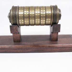 May include: A brass cipher wheel with rotating lettered rings, mounted on a dark wooden base. The antique-style encryption device features engraved details and is supported by two wooden uprights. The letters are arranged in a seemingly random order.