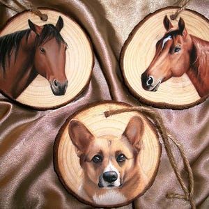 May include: Three wooden ornaments with painted images of animals. The first ornament features a brown horse with a black mane and tail. The second ornament features a brown horse with a white stripe on its face. The third ornament features a brown and white corgi dog.
