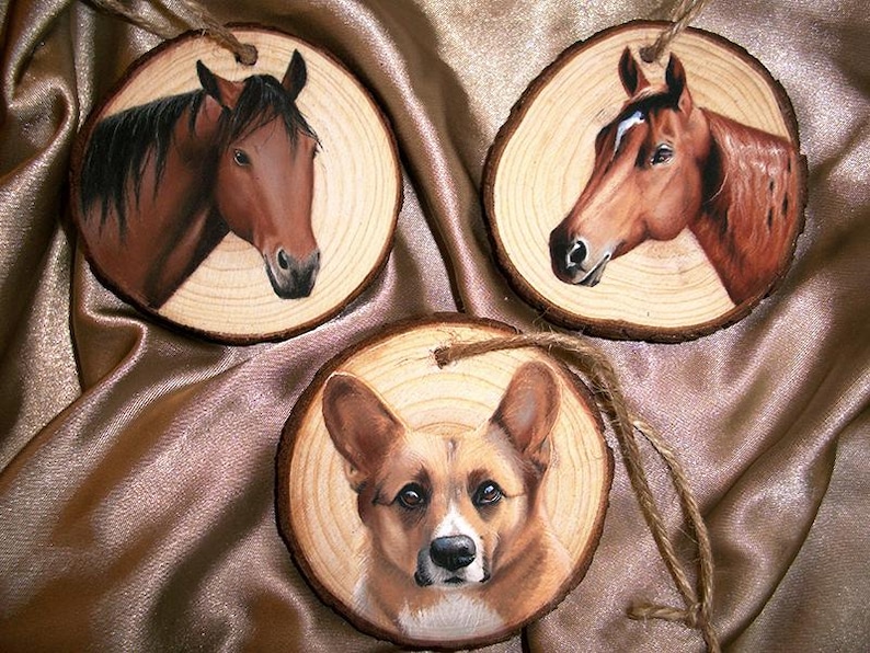 May include: Three wooden ornaments with painted images of animals. The first ornament features a brown horse with a black mane and tail. The second ornament features a brown horse with a white stripe on its face. The third ornament features a brown and white corgi dog.