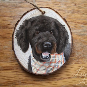 May include: A hand-painted wooden ornament featuring a black dog with a plaid bandana. The ornament is round and has a rustic wood grain texture.