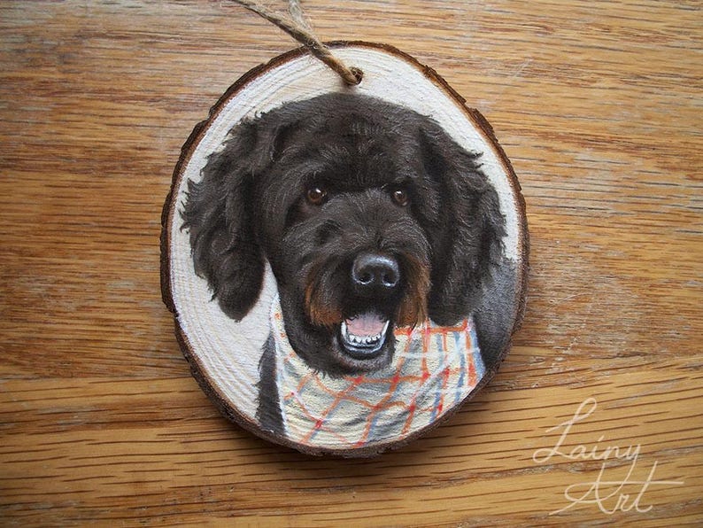 May include: A hand-painted wooden ornament featuring a black dog with a plaid bandana. The ornament is round and has a rustic wood grain texture.