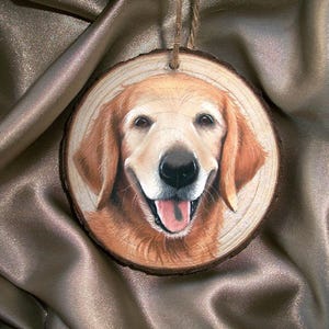 May include: A hand-painted wooden ornament featuring a golden retriever dog with a happy expression. The dog is painted realistically with brown fur and a pink tongue.