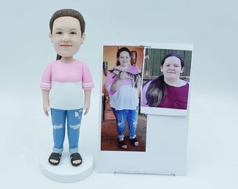 May include: A custom bobblehead figurine of a person wearing a pink and white shirt, blue jeans, and black sandals. A photo of the person holding a fish is next to the figurine.