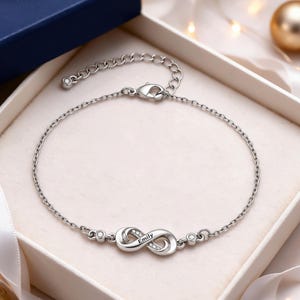 Op de afbeelding: Een zilverkleurige kettingarmband met een oneindigheidssymbool waarin de naam Emily is gegraveerd. Het oneindigheidssymbool is aan één kant versierd met kleine heldere steentjes. De armband heeft een karabijnsluiting en een verlengketting.