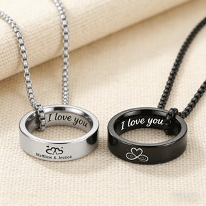 以下が含まれることがあります： 2つのマッチングリングネックレス。1つは「I love you」と刻印され、「Matthew & Jessica」の名前が2つのハートの下に書かれたシルバーです。もう1つは「I love you」と無限のハートのシンボルが付いた黒です。