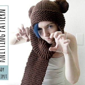 May include: A brown knitted hat with bear ears and a matching scarf. The hat has a hood and the scarf is long and wide. The person wearing the hat and scarf is making a claw-like gesture with both hands.
