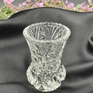 May include: A clear, small glass vase with a detailed, textured pattern. The vase has a flared top and a rounded base. The design features diamond and geometric shapes. The vase is likely for decorative purposes.
