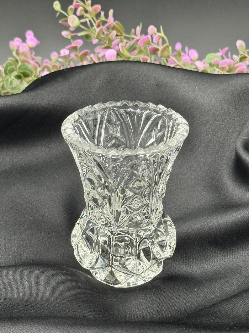 May include: A clear, small glass vase with a detailed, textured pattern. The vase has a flared top and a rounded base. The design features diamond and geometric shapes. The vase is likely for decorative purposes.