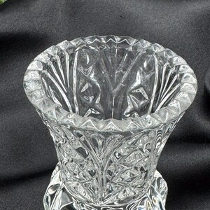May include: A clear, cut-glass vase with a wide, scalloped rim and a detailed, textured pattern. The vase has a flared shape and a decorative base. The intricate design catches the light, creating a sparkling effect. The vase is likely for decorative purposes.