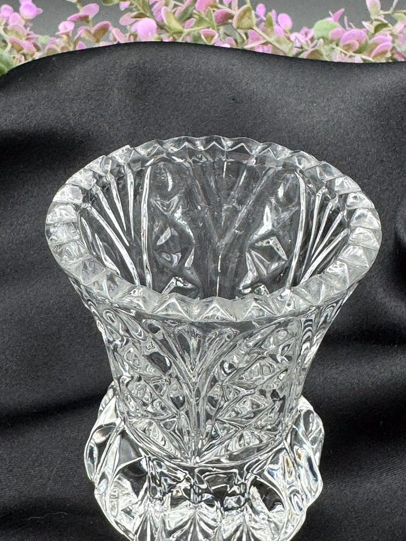 May include: A clear, cut-glass vase with a wide, scalloped rim and a detailed, textured pattern. The vase has a flared shape and a decorative base. The intricate design catches the light, creating a sparkling effect. The vase is likely for decorative purposes.