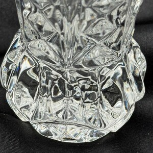 May include: A clear, cut-glass vase with a detailed, geometric pattern. The vase has a wide, scalloped base and a flared top. The intricate design reflects light, creating a sparkling effect. The vase is likely used for decorative purposes.