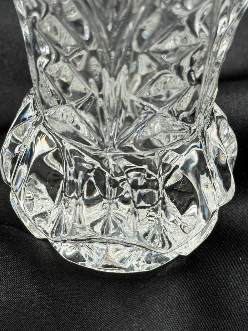 May include: A clear, cut-glass vase with a detailed, geometric pattern. The vase has a wide, scalloped base and a flared top. The intricate design reflects light, creating a sparkling effect. The vase is likely used for decorative purposes.