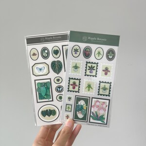 K&ouml;nnte beinhalten: Zwei Stickerb&ouml;gen mit botanischen Illustrationen. Ein Bogen hat ovale und rechteckige Aufkleber mit Bildern von Bl&auml;ttern und einem Schmetterling. Der andere Bogen hat stempelf&ouml;rmige Aufkleber mit floralen Designs. Der Markenname "Ripple Botanic" ist oben auf jedem Bogen aufgedruckt.