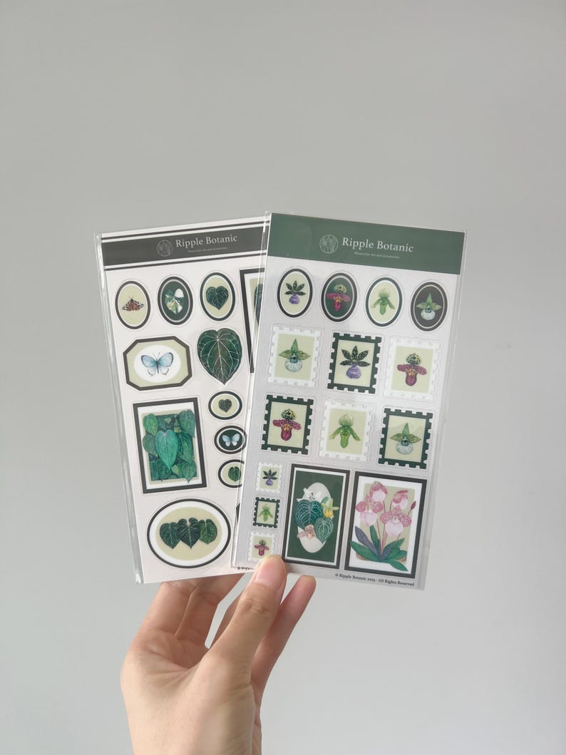 K&ouml;nnte beinhalten: Zwei Stickerb&ouml;gen mit botanischen Illustrationen. Ein Bogen hat ovale und rechteckige Aufkleber mit Bildern von Bl&auml;ttern und einem Schmetterling. Der andere Bogen hat stempelf&ouml;rmige Aufkleber mit floralen Designs. Der Markenname "Ripple Botanic" ist oben auf jedem Bogen aufgedruckt.