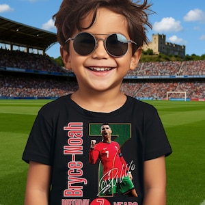 May include: A black t-shirt featuring a soccer player in a red jersey with the number 7. The shirt has the text "Bryce-Noah" and "Birthday Boy 7 Years" in red. The boy in the image is wearing sunglasses and smiling.