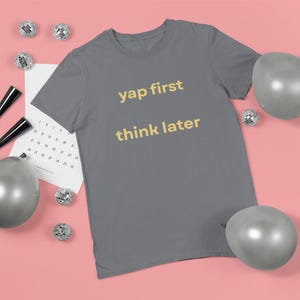 May include: A gray t-shirt with the text "yap first think later" in a yellow font. The shirt is surrounded by silver balloons, disco balls, and a calendar on a pink background.