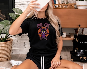 May include: Black t-shirt and shorts set with the text "EVIL CAT" and a cartoon cat graphic. The cat is purple with yellow eyes and is set against an orange background. The shorts have a white drawstring.