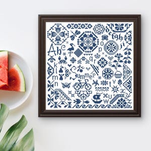 Könnte beinhalten: Ein gerahmtes Kreuzstich-Exemplar in einem dunkelbraunen Rahmen. Das Exemplar zeigt verschiedene blaue und weiße Muster, darunter Buchstaben, Blumen und ein Fahrrad. Das Wort "Summer" ist in der Mitte gestickt. Wassermelonenscheiben liegen auf einem weißen Teller.