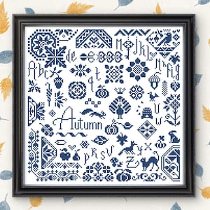 以下が含まれることがあります： 黒いフレームに入ったクロスステッチのサンプル。デザインは、どんぐり、カボチャ、葉など、すべて青色の秋をテーマにしたさまざまなモチーフが特徴です。「Autumn」の文字は筆記体でステッチされています。背景は葉の模様のクリーム色です。
