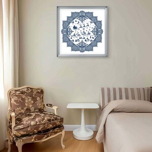 May include: A framed, blue and white cross-stitch artwork depicting a winter scene with Santa's sleigh, reindeer, and a village. The artwork is in a silver frame and hangs on a beige wall. A patterned chair and a white side table are in the foreground.
