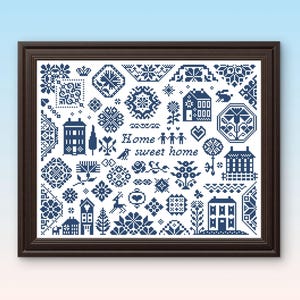 May include: Framed cross-stitch art featuring a collection of blue and white folk art motifs. The design includes houses, flowers, and geometric patterns, with the words "Home sweet home" in the center. The frame is dark brown.