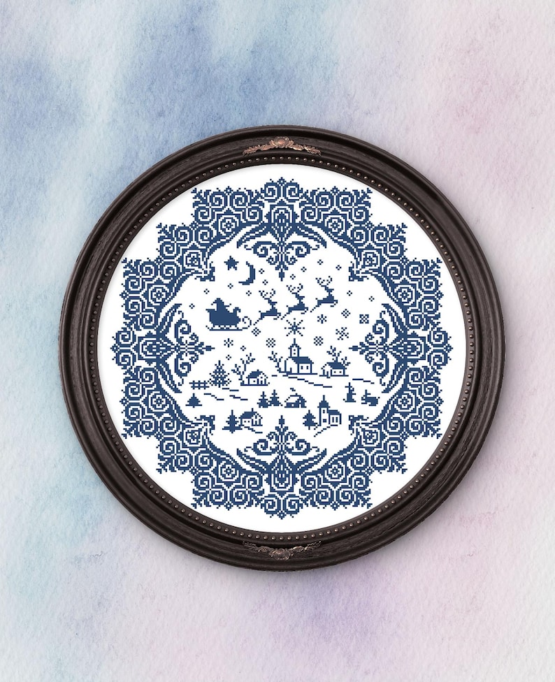 May include: A framed cross-stitch depicting a winter village scene in shades of blue and white. The design features a detailed border, a crescent moon, stars, Santa Claus in a sleigh, reindeer, houses, and trees. The frame is dark brown.