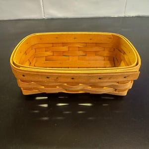 May include: A rectangular woven basket made of light brown wood strips. The basket features a classic interlaced pattern with a reinforced rim and small dark metal fasteners securing the overlapping ends of the wood strips along the exterior.