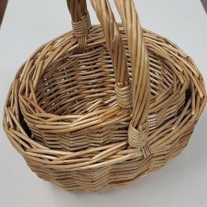 May include: A set of three woven wicker baskets with a single handle. The baskets are nested inside each other, with the largest basket at the bottom and the smallest basket at the top.