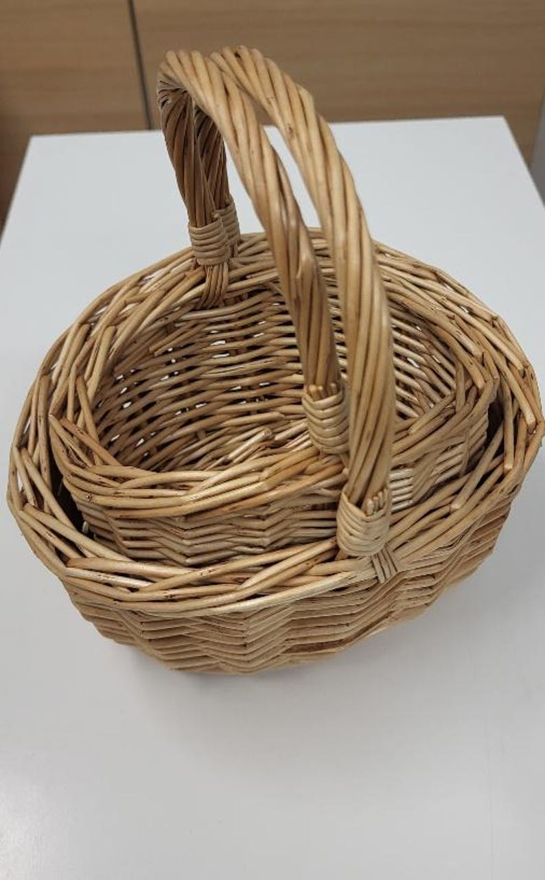 May include: A set of three woven wicker baskets with a single handle. The baskets are nested inside each other, with the largest basket at the bottom and the smallest basket at the top.