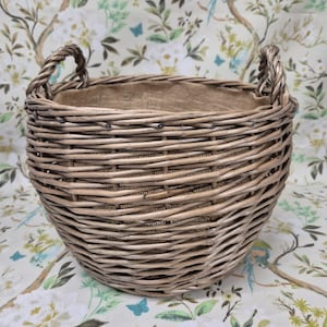 May include: A round wicker basket with two braided handles. The basket is a natural light brown colour and is lined with a hessian fabric. The basket is suitable for storage or display.