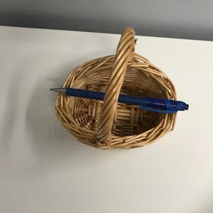May include: A woven wicker basket with a handle. The basket is oval shaped and has a natural brown color.