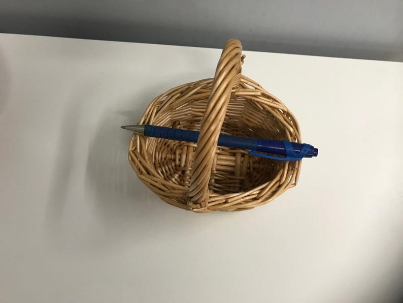 May include: A woven wicker basket with a handle. The basket is oval shaped and has a natural brown color.