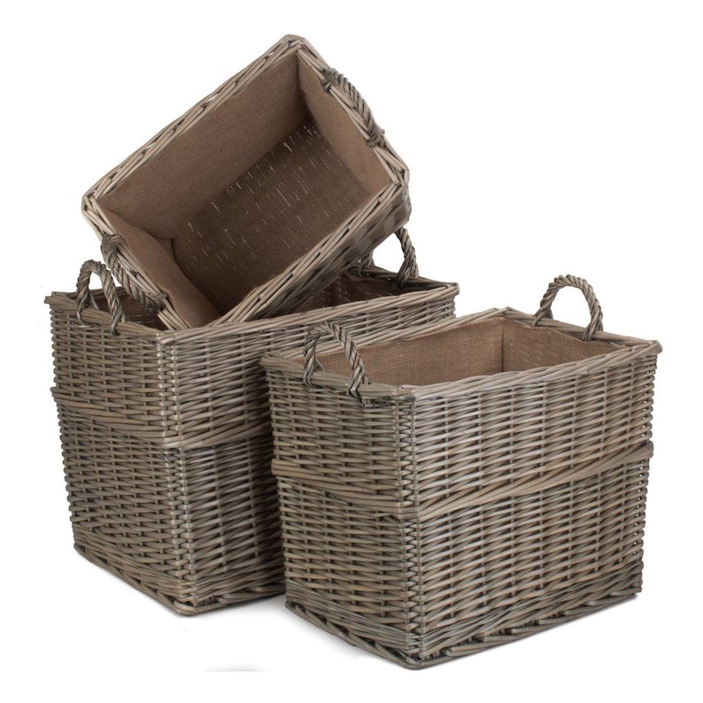 May include: Three rectangular woven wicker baskets in varying sizes. The baskets are a natural gray color and have a burlap lining. Each basket has two curved handles for easy carrying. The baskets are stacked, with one partially inside another.