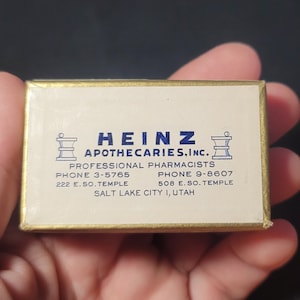 May include: A gold box with a white label that reads "HEINZ APOTHECARIES, INC." with two phone numbers and addresses for a pharmacy in Salt Lake City, Utah.