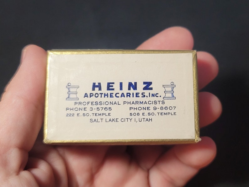 May include: A gold box with a white label that reads "HEINZ APOTHECARIES, INC." with two phone numbers and addresses for a pharmacy in Salt Lake City, Utah.