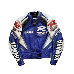K&ouml;nnte beinhalten: Blaue, wei&szlig;e und schwarze Yamaha Motorradjacke mit "R"- und "Yamaha"-Logos. Die Jacke hat einen Rei&szlig;verschluss vorne, gepolsterte Schultern und einen Stehkragen. Die &Auml;rmel tragen das Yamaha-Logo.