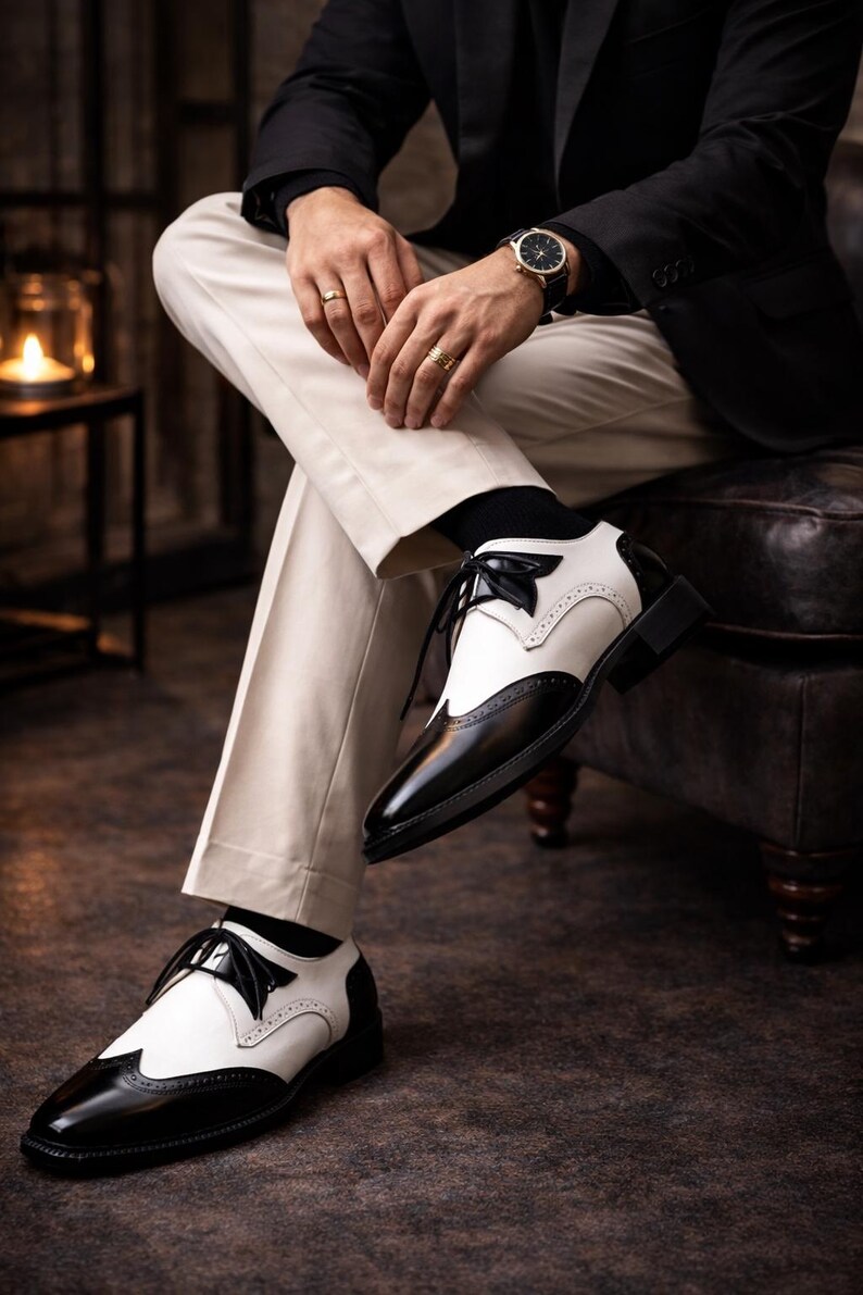May include: Black and white spectator shoes with a classic design. The shoes feature a two-tone color scheme, with black leather and white accents. The shoes have a lace-up closure and a low heel. The shoes are part of a formal wear collection.