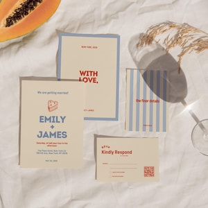 May include: A set of wedding stationery in cream and blue. The invitations and RSVP cards feature text, including "Emily + James" and "With Love." A slice of papaya and a glass are also visible. The stationery is arranged on a white surface.