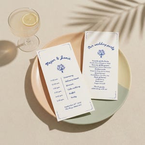 May include: Two wedding ceremony programs with blue floral illustrations and text on a two-tone plate. One program reads "Megan & Jamie" with a schedule. The other says "Our wedding party" with names. A cocktail with a lemon slice is in the background.