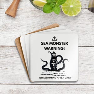 May include: A stack of square coasters with a cork base. The top coaster is white with a black graphic of a lighthouse with tentacles and the text "SEA MONSTER WARNING!" and "NO SWIMMING AFTER DARK".
