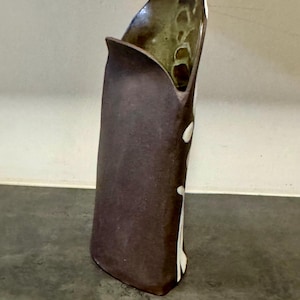 May include: A tall, dark brown ceramic vase with a unique, asymmetrical shape. The vase has a curved opening and a textured surface. White, irregular shapes decorate the side. The interior is a lighter brown with a glossy finish. A decorative home accent.
