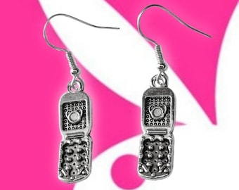 May include: Silver-toned dangle earrings shaped like flip phones. Each earring features a detailed design of a phone with a keypad and screen, suspended from a simple hook. The earrings are set against a pink and white background.