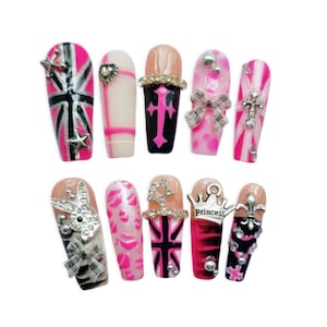 Könnte beinhalten: Ein Set aus zehn künstlichen Fingernägeln mit verschiedenen Designs, darunter pink-schwarze Union-Jack-Muster, karierte Schleifen, silberne Anhänger in Form eines Hasen, eine Krone mit dem Wort princess, ein Kreuz, eine Lilie sowie Lippenabdrücke.
