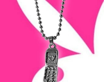 May include: Silver-toned pendant necklace featuring a detailed flip phone charm. The charm is suspended from a ball chain. The background is a vibrant pink and white design.