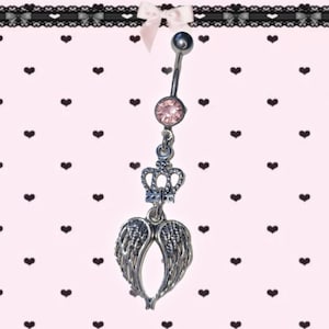 May include: A silver belly button ring with a pink gem, a crown, and a pair of angel wings. The ring has a curved barbell design. The background is pink with black hearts.