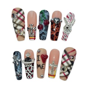 May include: A collection of ten artificial nails with diverse designs. The nails showcase patterns including plaid, leopard print, and lace, embellished with crosses, hearts, and rhinestones. Some nails feature the text "I ME".