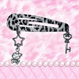 May include: A patterned hair clip in black and white, with silver charms. The charms are a star, a skull and crossbones, and a key. The clip is a barrette style, with a leopard print design.