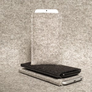 Puede incluir: Dos fundas de teléfono de fieltro apiladas una encima de la otra. La funda superior es de color gris claro y la inferior es de color gris oscuro. Ambas fundas están hechas de un material suave y peludo.